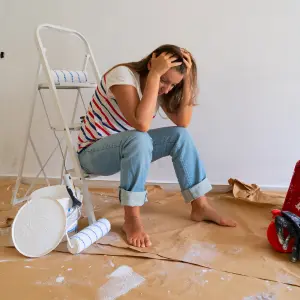 Stressed woman sitting amidst renovation materials, illustrating the challenges and hassles of home rehab and renovation, particularly relevant for those inheriting property and seeking to avoid these burdens.