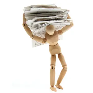 A wooden mannequin is struggling to carry a heavy pile of papers, symbolizing the burden of dealing with maintenance issues and back taxes when owning a property.