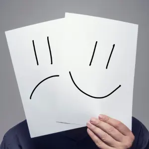 A man holds up two pieces of paper with contrasting facial expressions: a sad face and a happy face. This symbolizes the emotional rollercoaster of selling an inherited property, highlighting the potential challenges and rewards involved.