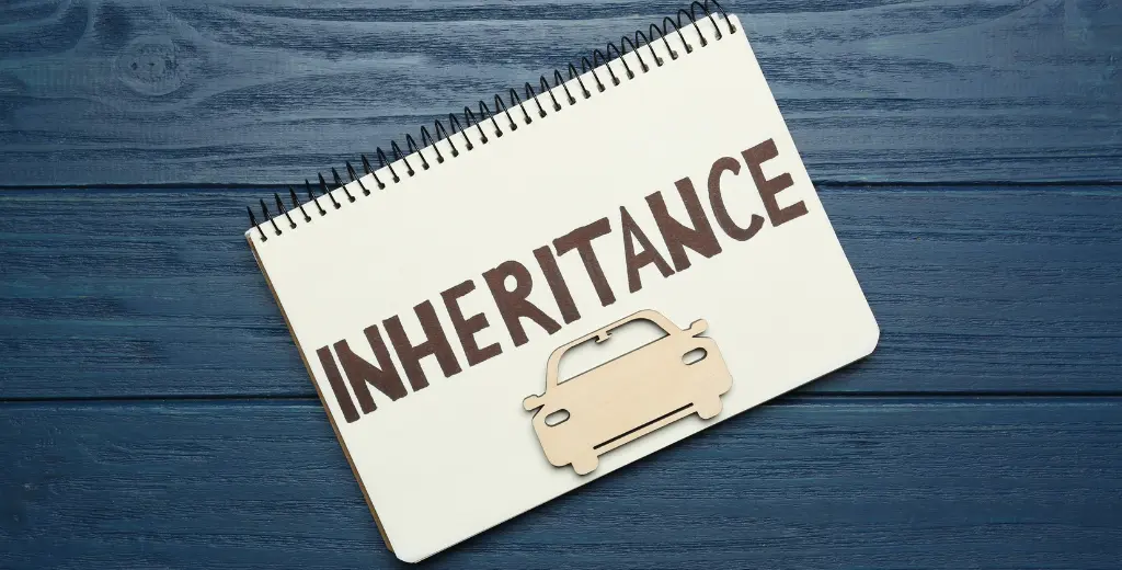 Notebook with the word 'Inheritance' written on it alongside a car cutout, symbolizing the process of inheriting assets such as property, relevant to discussions on selling an inherited house quickly for cash